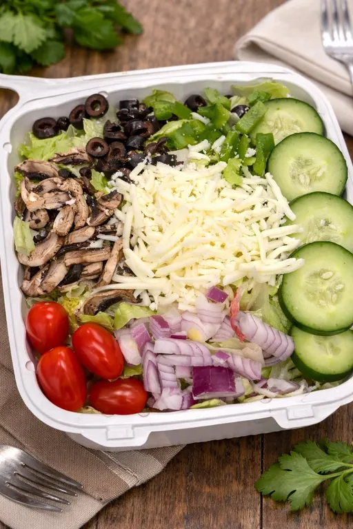 A fresh salad in a to-go box with cucumber, tomatoes, red onion, olives, mushrooms and shredded cheese